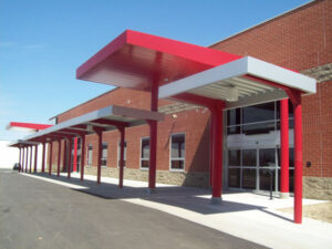 Modern brick building with red metal awnings and columns over a sidewalk by the entrance.