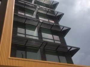 Modern building with large windows and sunshades, seen from below against a cloudy sky.