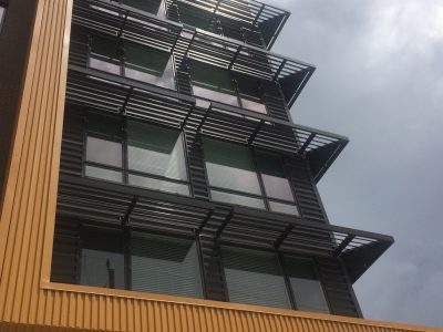 Modern building with large windows and sunshades, seen from below against a cloudy sky.