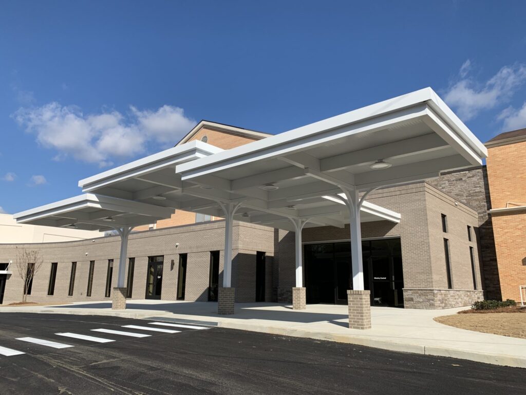 Modern building with a large covered entrance, brick walls, and a clear blue sky in the background.