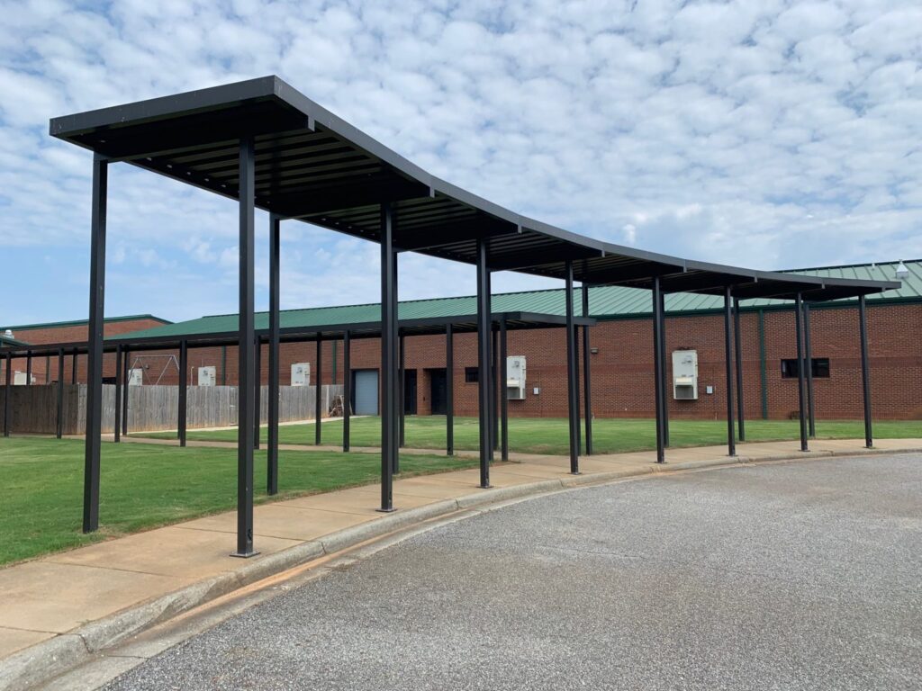 Covered walkway with black metal posts in front of a brick building on a partly cloudy day.